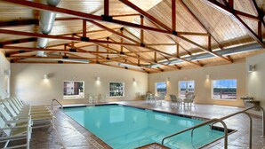 Ein überdachter Pool mit Fliesenboden, Holzbalken und Blick ins Freie durch große Fenster.