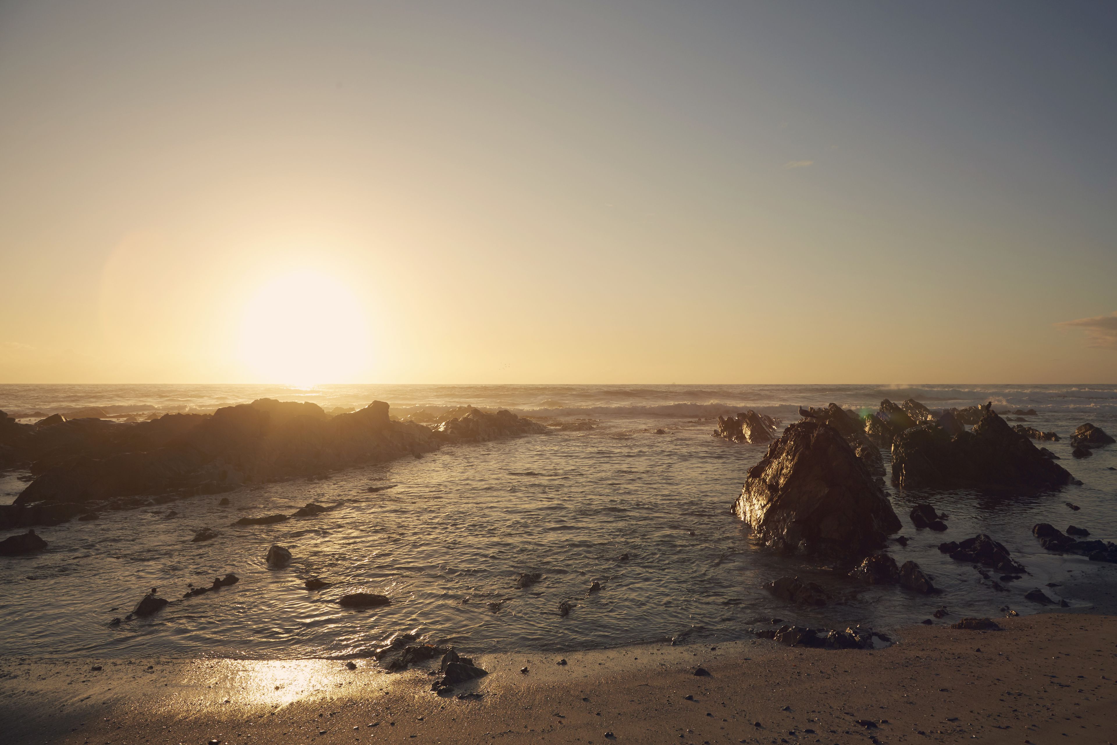 A beach with rocks and the sun setting in the background.