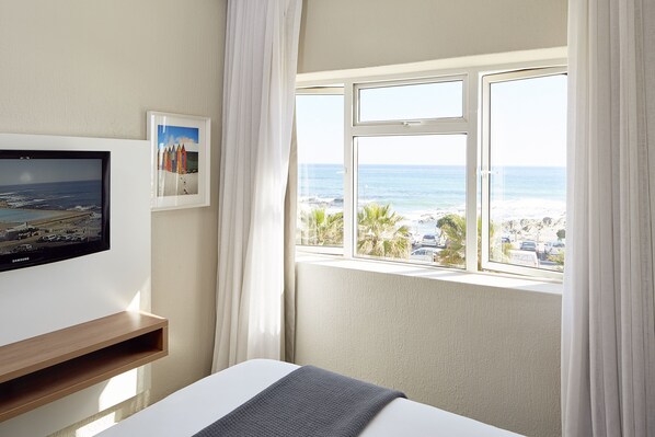 A hotel room with a bed, a TV, a window with a view of the beach, and a picture on the wall.