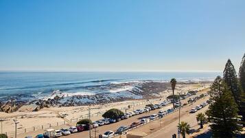 A coastal road with parked cars, a beach, and the ocean in the background.