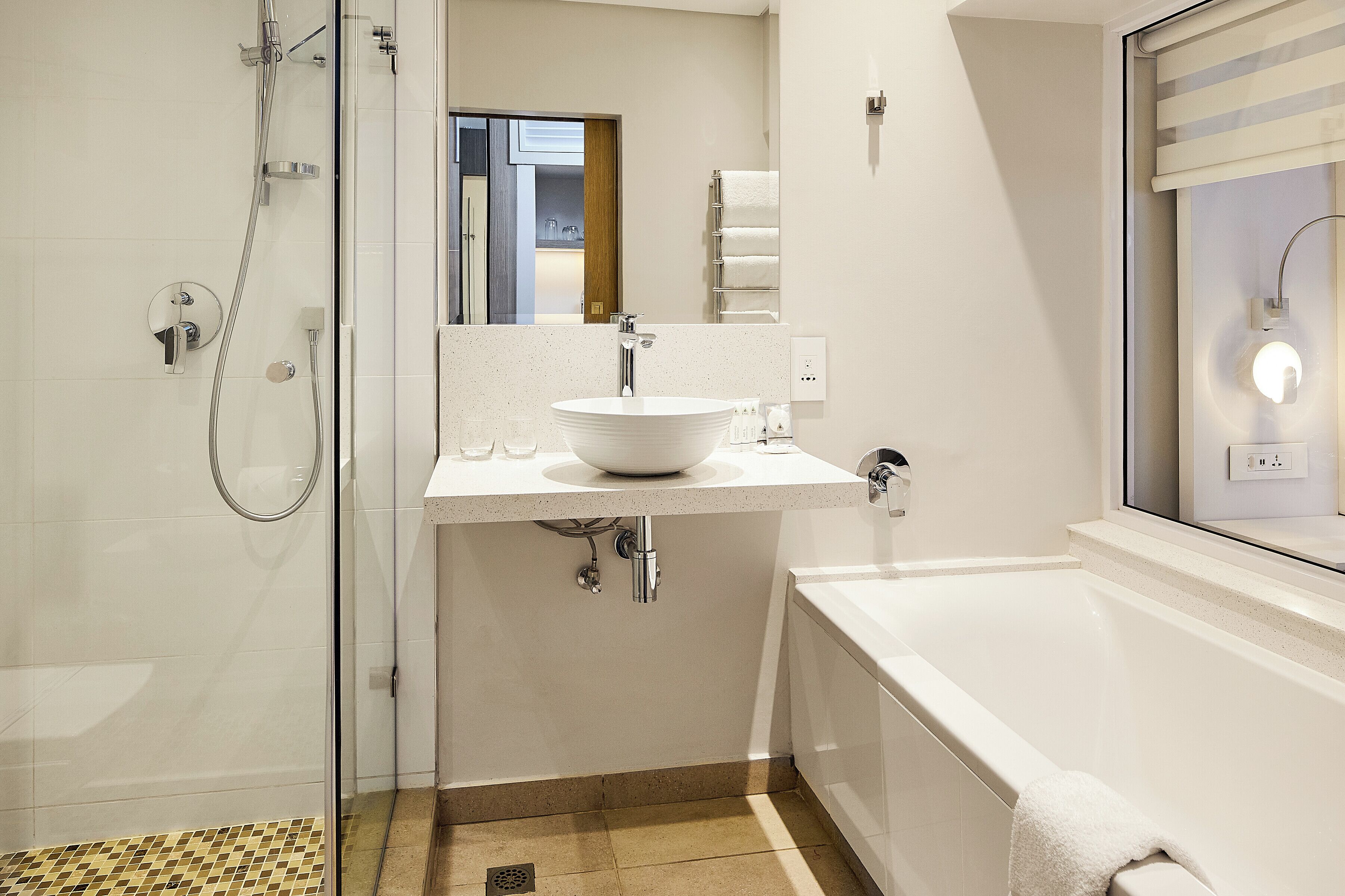A modern bathroom with a glass shower enclosure, a white sink with a vessel basin, and a standalone bathtub.