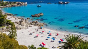 A beach with white sand, clear blue water, and large rocks. - First Group Riviera Suites (Cape Town)
