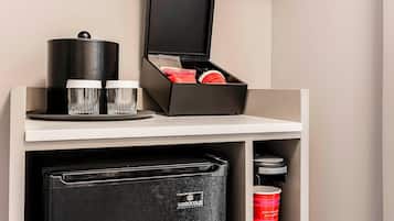 A minibar with a coffee machine, two glasses, and a container of cream.