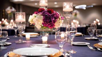 Une table dressée pour un dîner formel, avec des bougies, de la verrerie et un centre de table composé de fleurs.