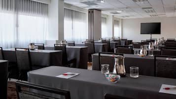 A conference room with multiple tables, chairs, and a large flat-screen TV on the wall.