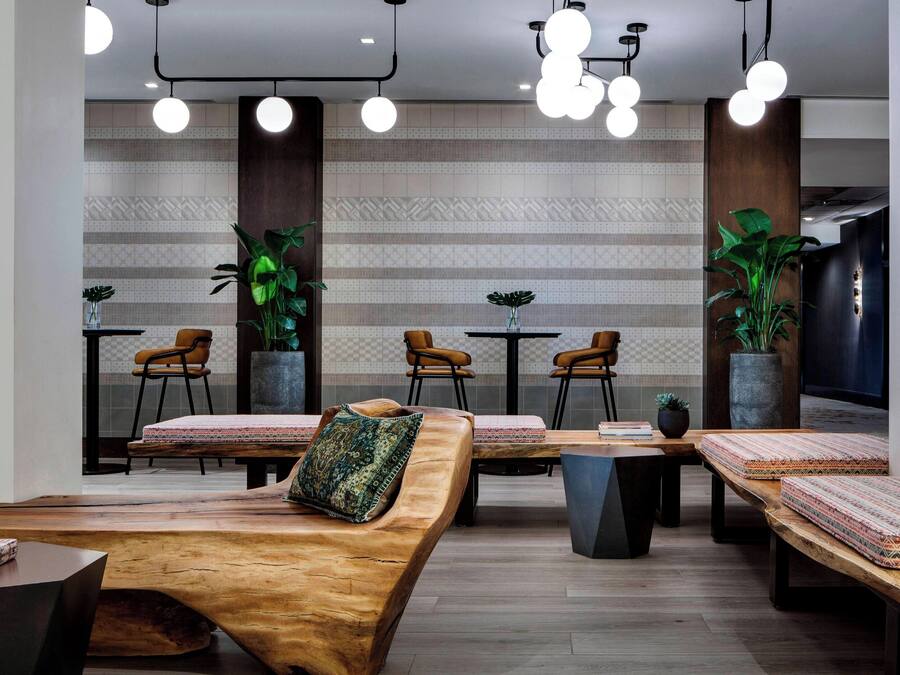 A modern interior with a wooden bench, tables, chairs, and hanging lights.