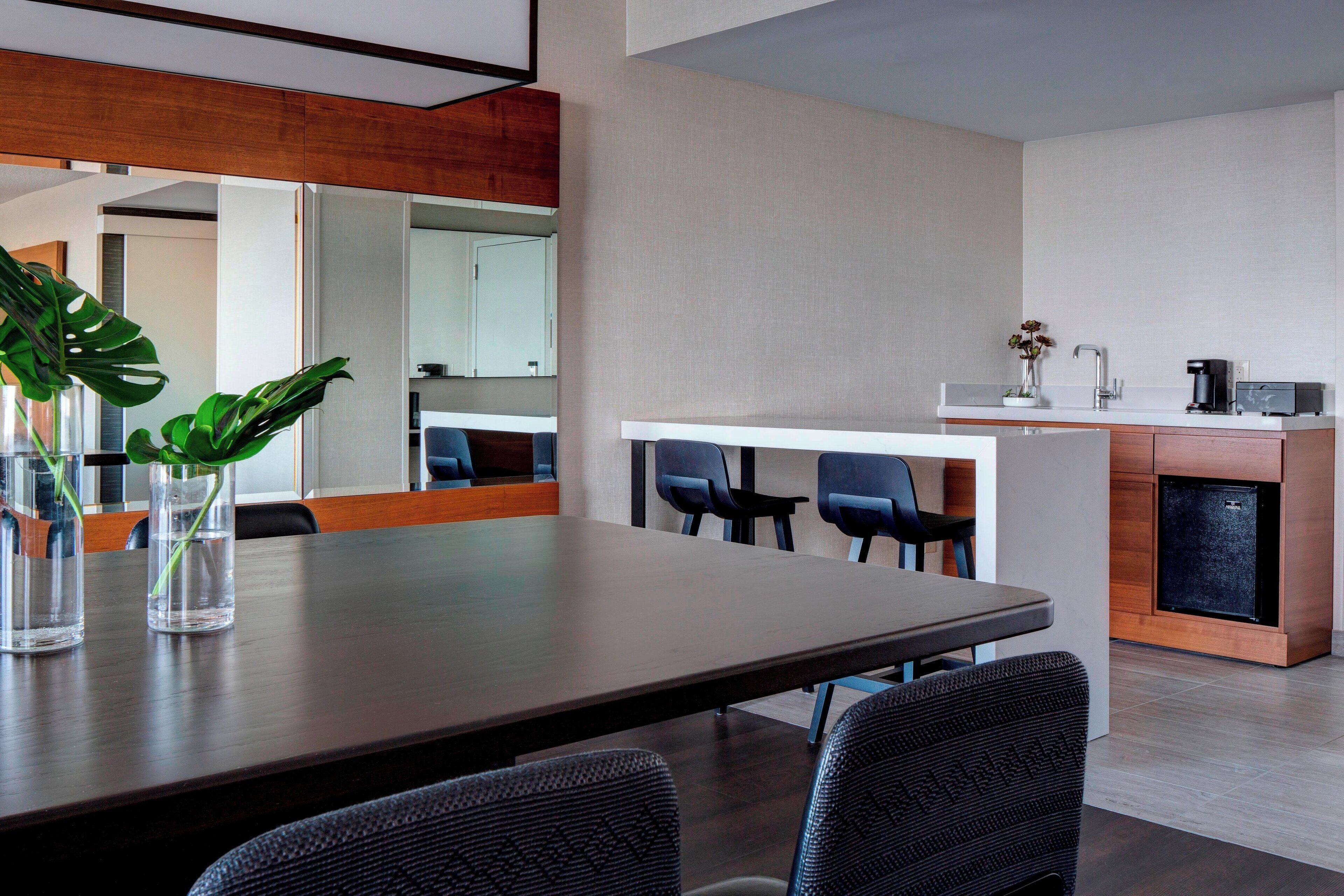 A modern conference room with a long table, several chairs, a coffee machine, and a small refrigerator.