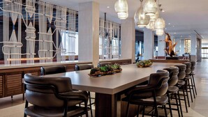 A modern hotel lobby with a long reception desk, black leather chairs, and decorative wall art. - New York LaGuardia Airport Marriott (East Elmhurst)