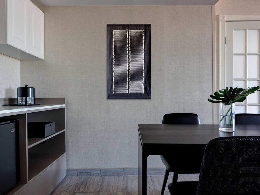 Una cocina compacta con refrigerador empotrado, cafetera y ventana con persianas.