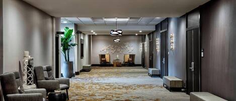 Vestíbulo de hotel con piso alfombrado, zona de estar con sillas, una recepción y una pared decorativa.