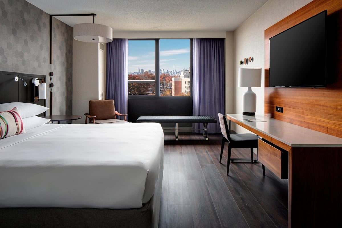 A hotel room with a large bed, a desk, a chair, a bench, and a TV.