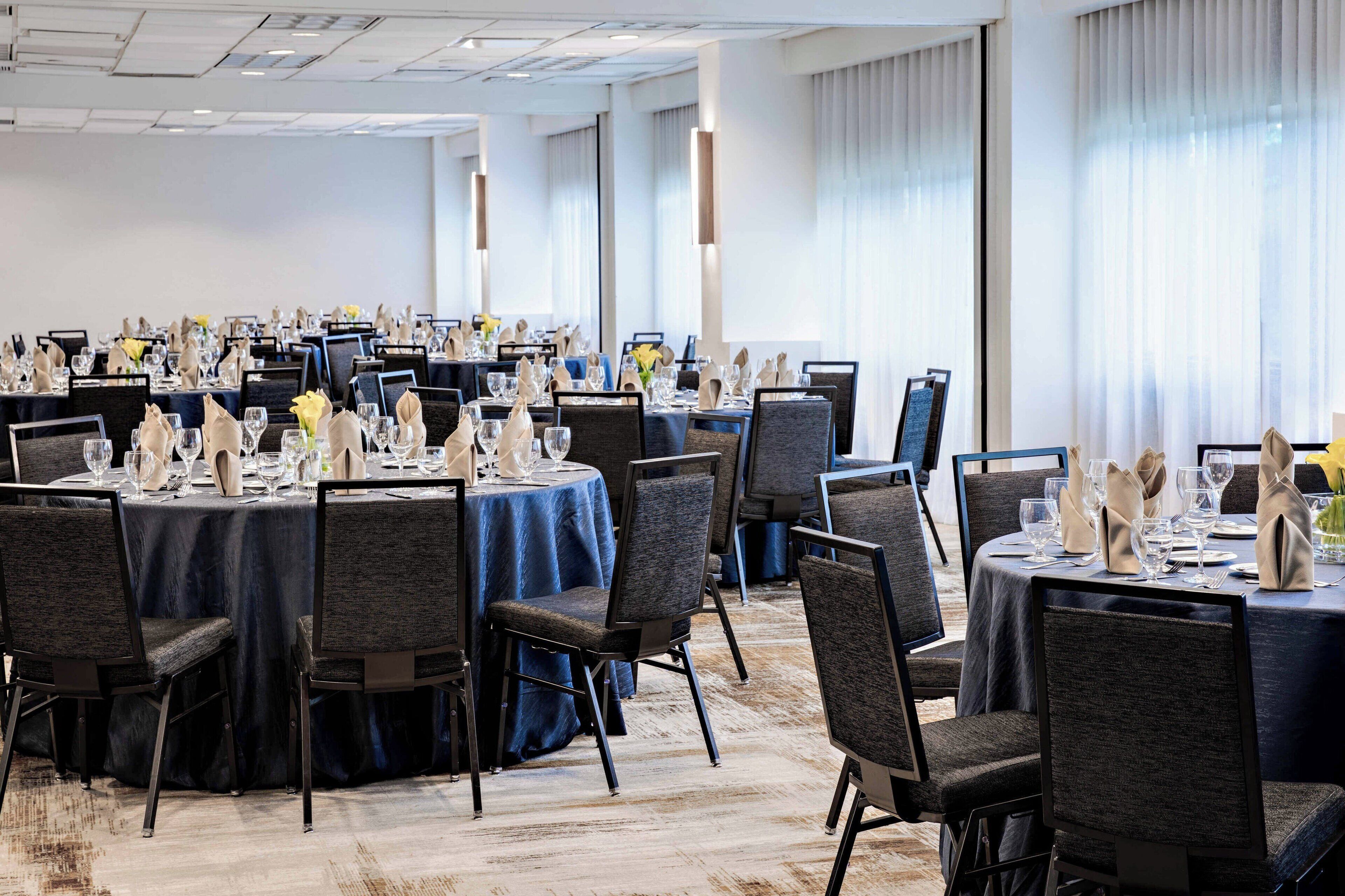 A banquet hall with round tables set for dining, featuring dark blue tablecloths and grey chairs.