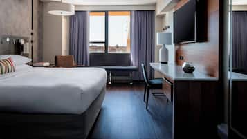 Una habitación de hotel con una cama grande, un escritorio, una silla, un televisor y una ventana con cortinas.