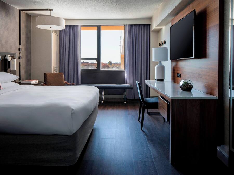 Una habitación de hotel con una cama grande, un escritorio, una silla, un televisor y una ventana con cortinas.