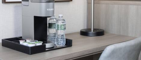 A hotel room with a coffee maker, water bottles, and a tray with tea and coffee pods.