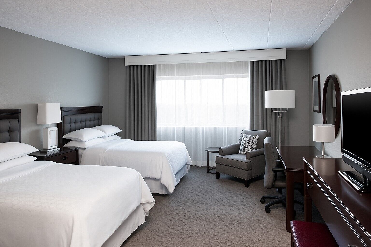A hotel room with two beds, a TV, a desk, and a chair.