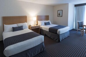 Two single beds with wooden headboards and dark bedspreads, a bedside table with a lamp and telephone, and a comfortable chair.