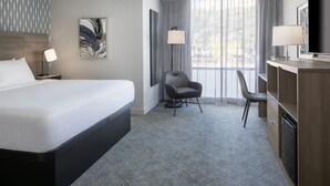 Habitación de hotel con una cama grande, un escritorio con una silla, televisión y ventana con cortinas.