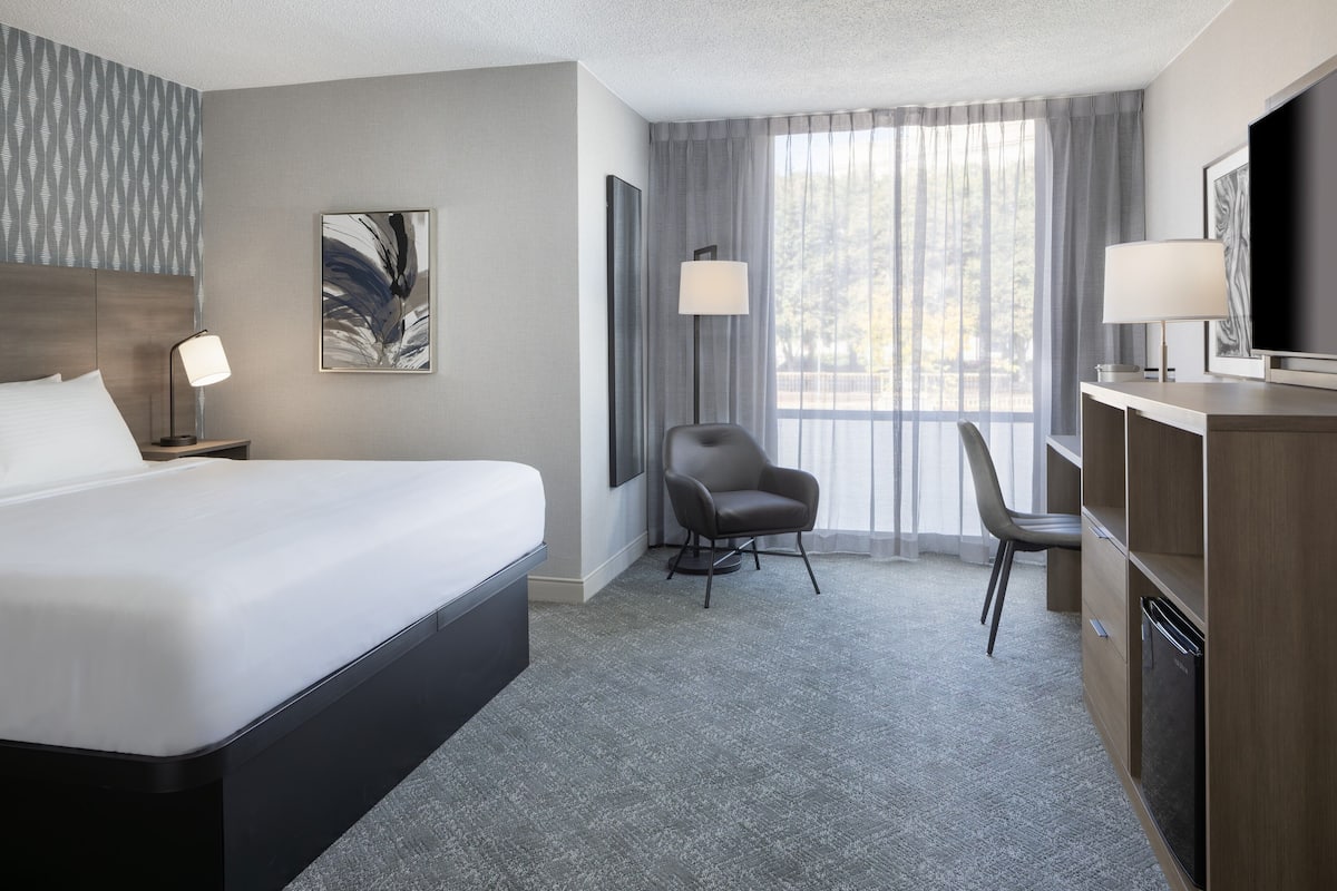 A hotel room with a large bed, a desk with a chair, a TV, and a window with curtains.