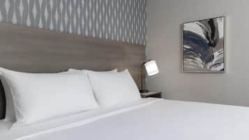 Una habitación de hotel con una cama grande, cabecera, mesita de noche con lámpara, y una pared con papel tapiz estampado y un cuadro.