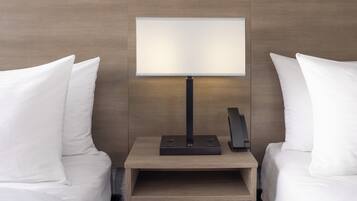 Una habitación de hotel moderna con cabecera de madera, una mesita de noche con lámpara y un teléfono.