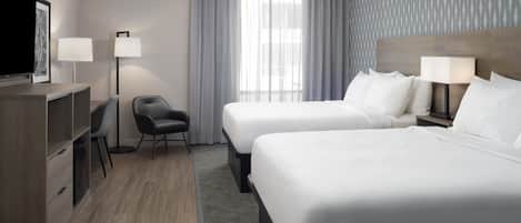 A hotel room with two beds, a desk, a chair, a TV, and a window with curtains.