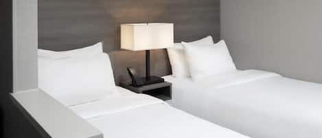 A hotel room with two single beds, a nightstand with a lamp, and a patterned wallpaper on the wall.