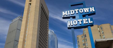 A sign for the Midtown Hotel with a modern architectural design, surrounded by high-rise buildings.