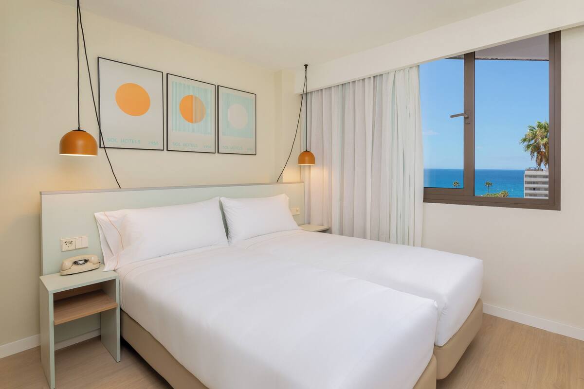 Une chambre d’hôtel avec un lit, une table de chevet, un téléphone et une fenêtre donnant sur la mer.
