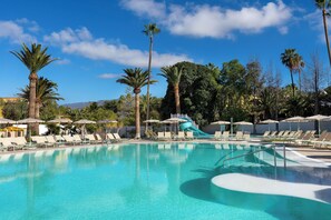 A swimming pool with a water slide, surrounded by palm trees and lounge chairs. - Sol Arona Tenerife (Arona)