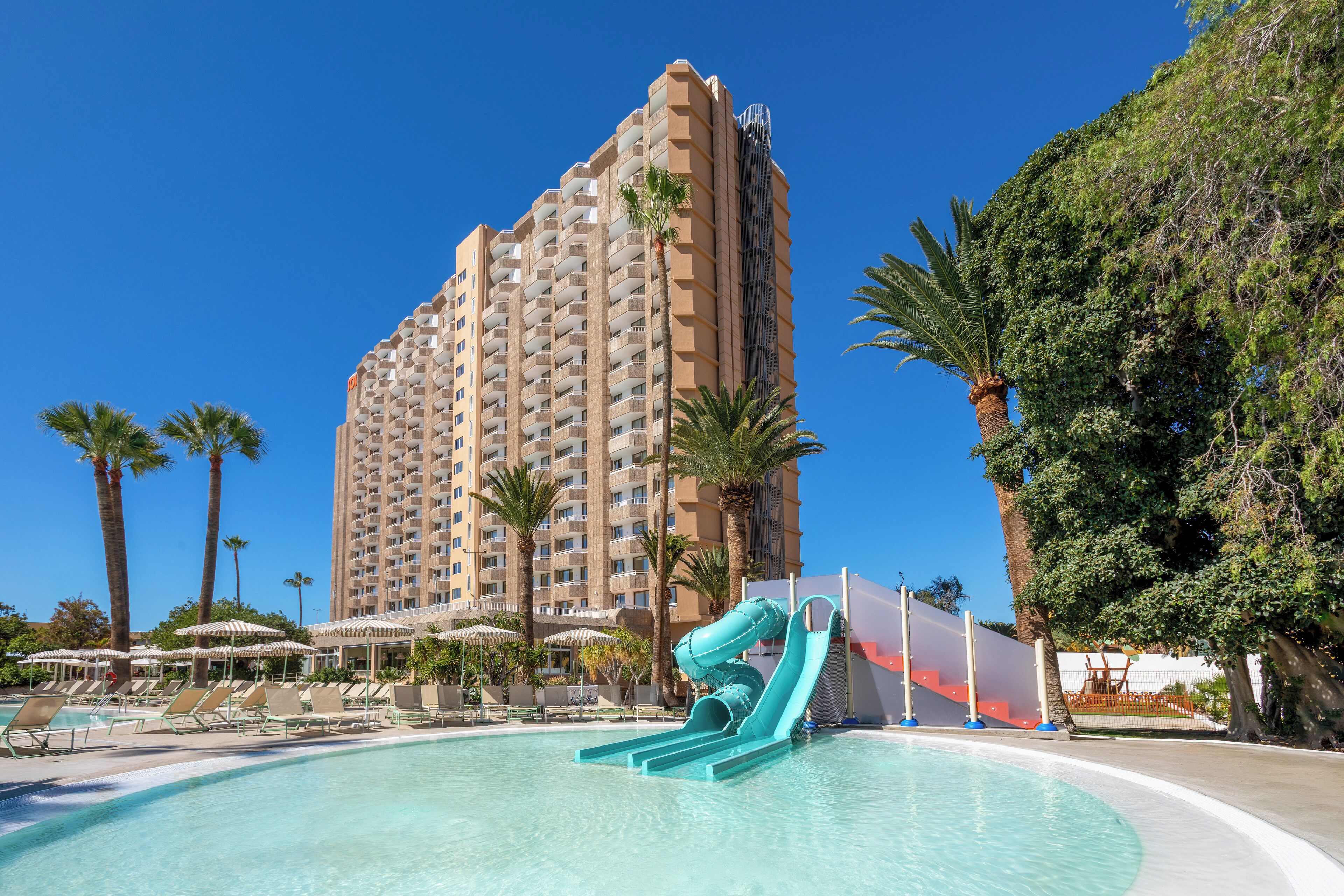 Un hôtel doté d’une piscine, d’un toboggan et de palmiers.