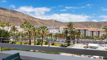 A balcony with a view of a coastal town, palm trees, and a mountain.