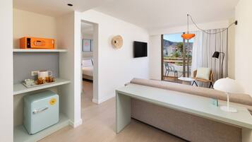 Una habitación de hotel moderna con sofá, una mesita, televisión y vistas al exterior.