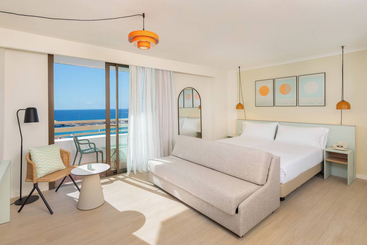 Une chambre d’hôtel avec un lit, un canapé, une petite table, une chaise, une table de chevet et une vue sur la mer.