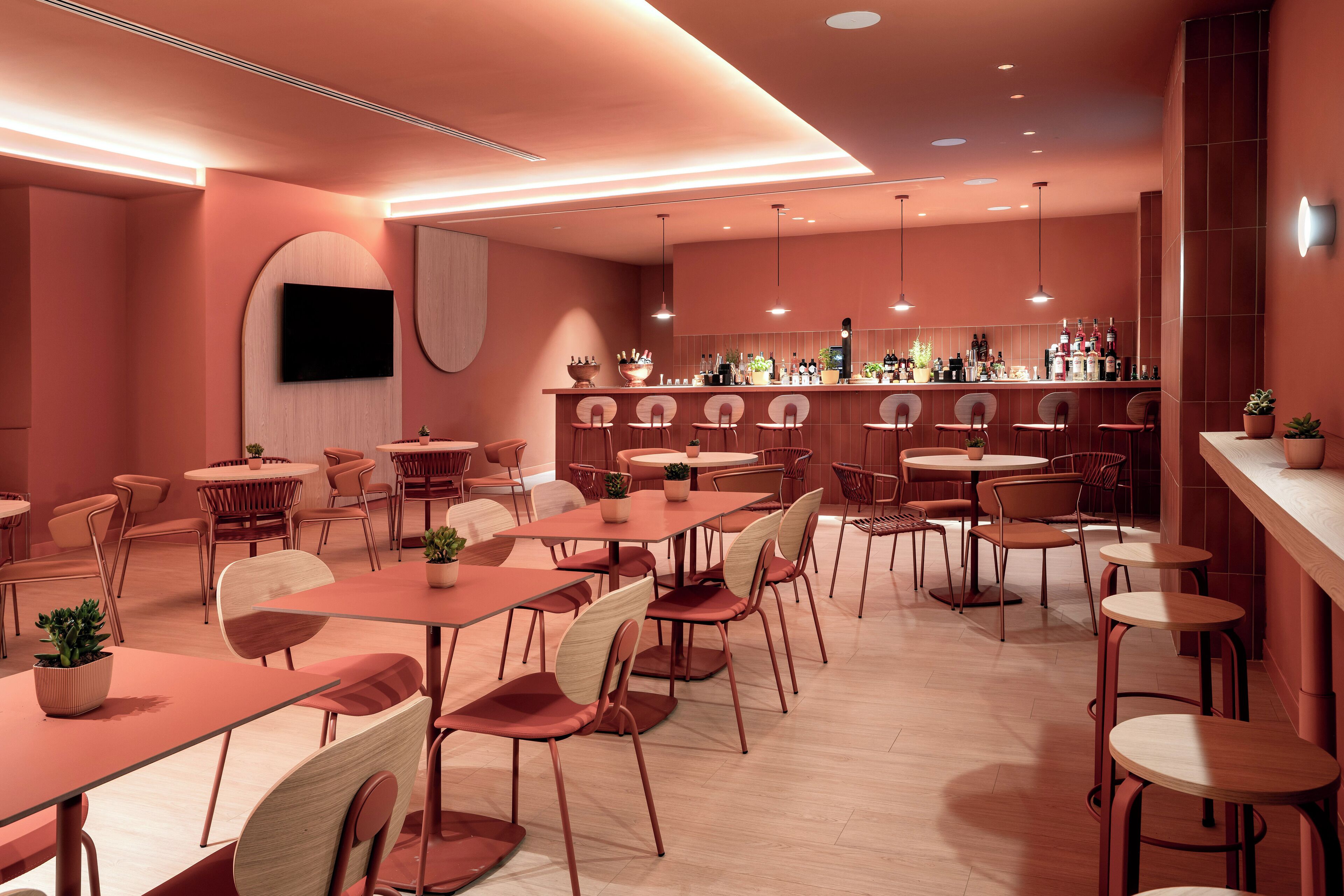 A modern restaurant with a bar area, multiple dining tables and chairs, and a flat-screen TV mounted on the wall.