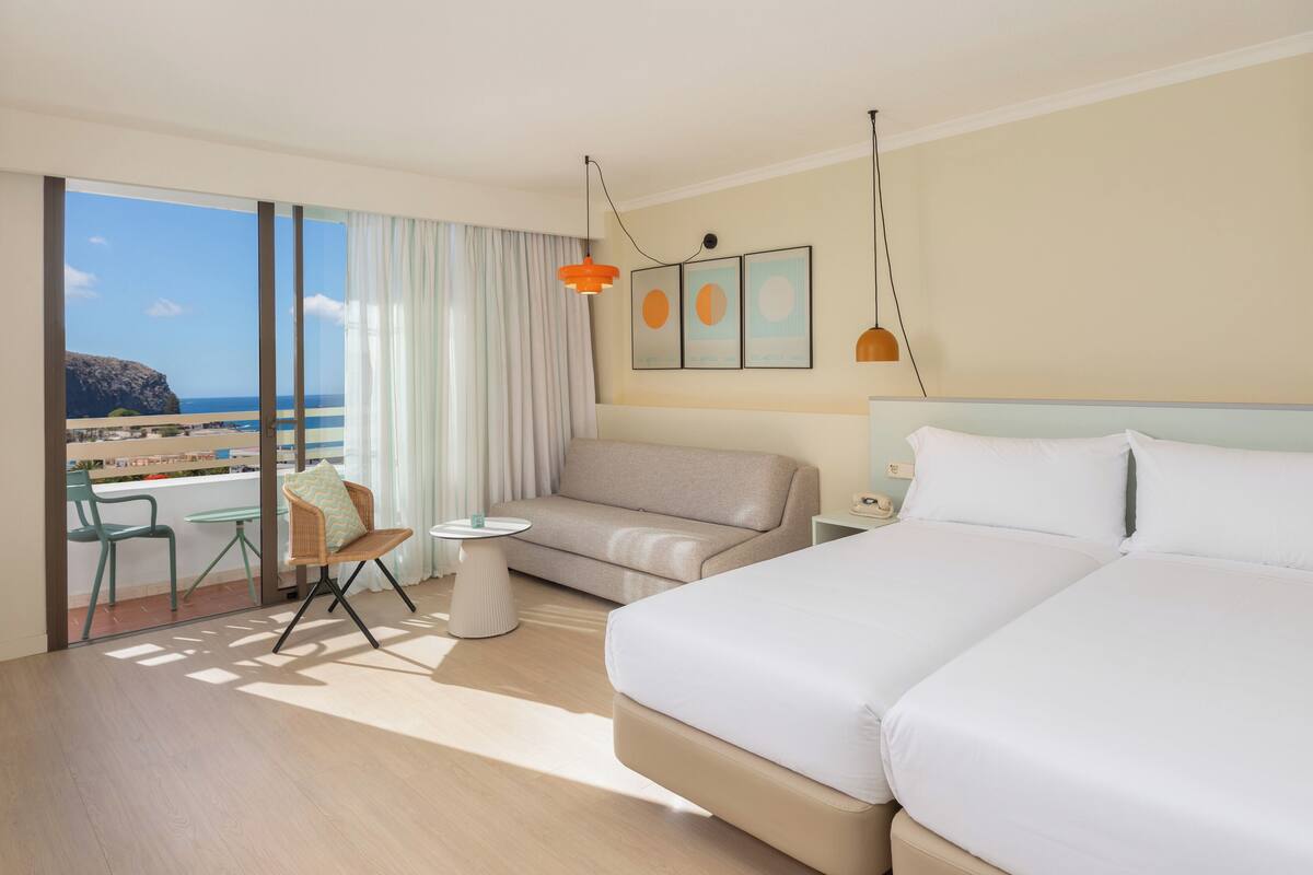 Une chambre d’hôtel avec un lit, un canapé, une petite table, une chaise et une vue sur la plage.