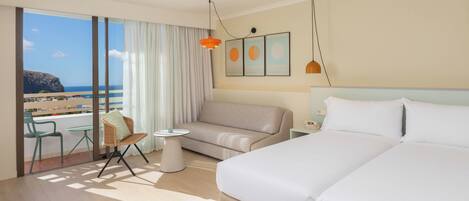 Ein Hotelzimmer mit Bett, einer Couch, einem kleinen Tisch, einem Sessel und Blick auf den Strand.
