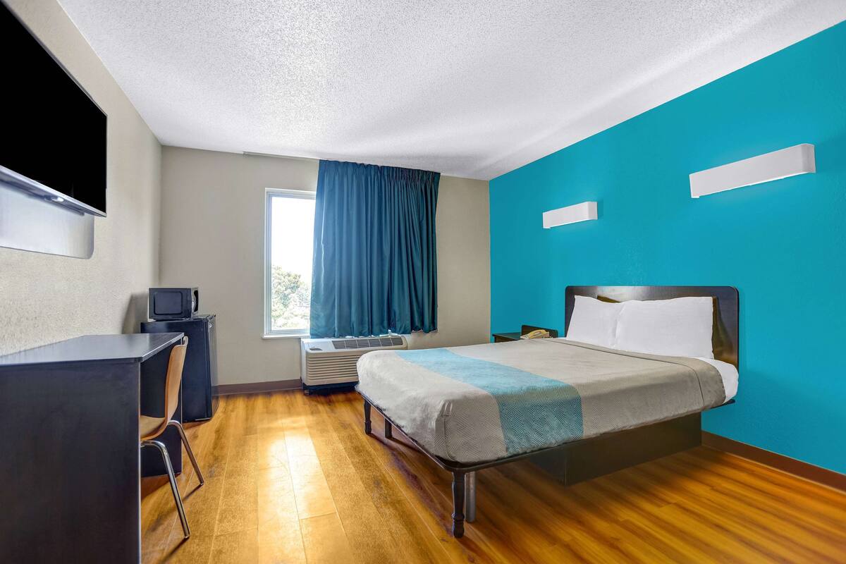 A hotel room with a bed, a desk, a television, and a window with curtains.