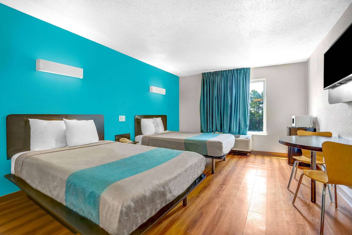 A hotel room with two beds, a dining table, and a TV.