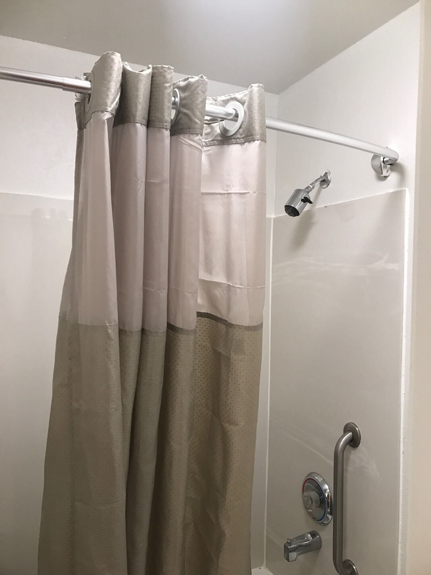 A shower area with a beige and white shower curtain, a handheld showerhead, and a wall-mounted faucet.