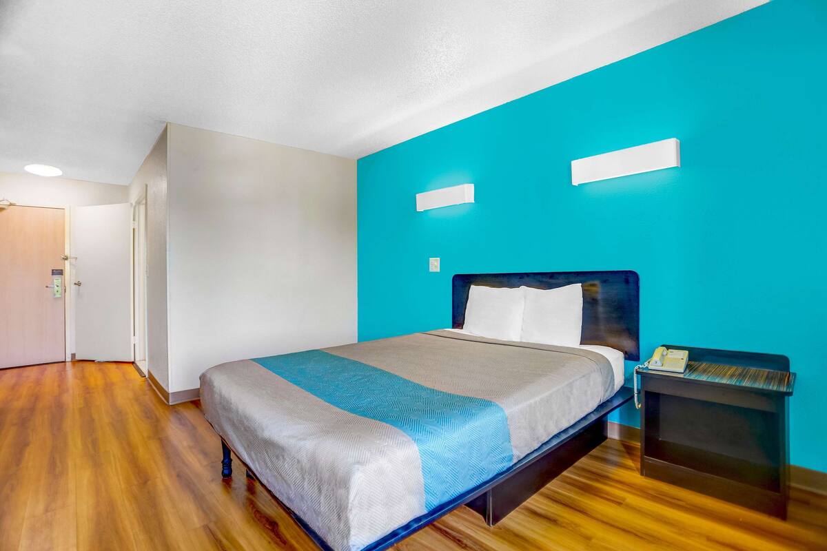 A neatly made bed with a blue and white bedspread, a wooden floor, and a nightstand with a phone.