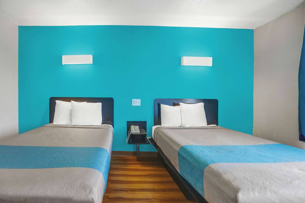 A hotel room with two beds, teal walls, and a wooden floor.