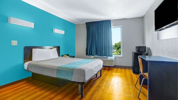 A hotel room with a bed, a desk, a chair, a TV, and a window with curtains. - Motel 6 Raleigh, NC - North (Raleigh)
