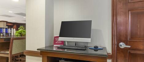 A reception desk with a computer, keyboard, and mouse. There is a printer and a sign that reads "ASSIST AVAIL UPON REQUEST."
