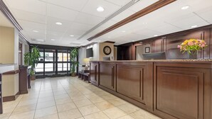 A reception area with a wooden reception desk, a clock, and a vase of flowers. - Best Western Dulles Airport Inn (Sterling)
