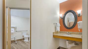 A bathroom with a wooden floor, a white toilet, a sink with a granite countertop, and a mirror with wall sconces.