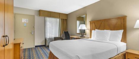 A hotel room with a large bed, a desk with a chair, a lamp, and a wardrobe.