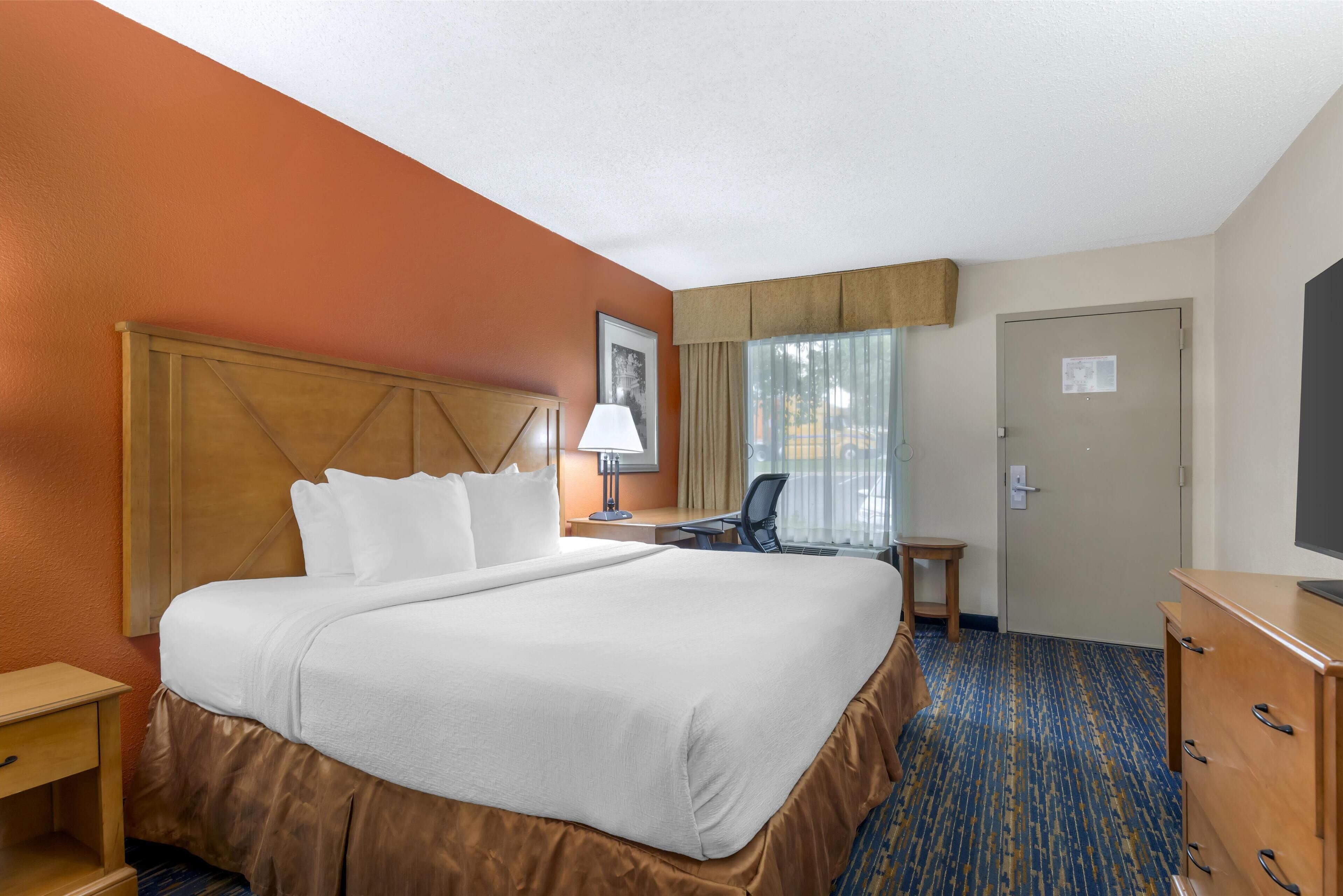 A hotel room with a large bed, a desk with a chair, a television, and a door.
