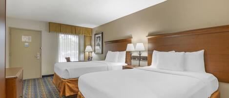 A hotel room with two beds, a wooden headboard, a desk, and a window with curtains.