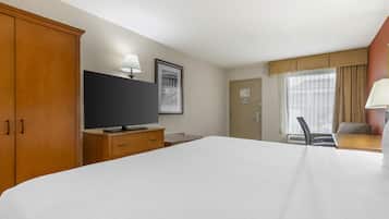 A hotel room with a large bed, a television, a desk with a lamp, and a window with curtains.